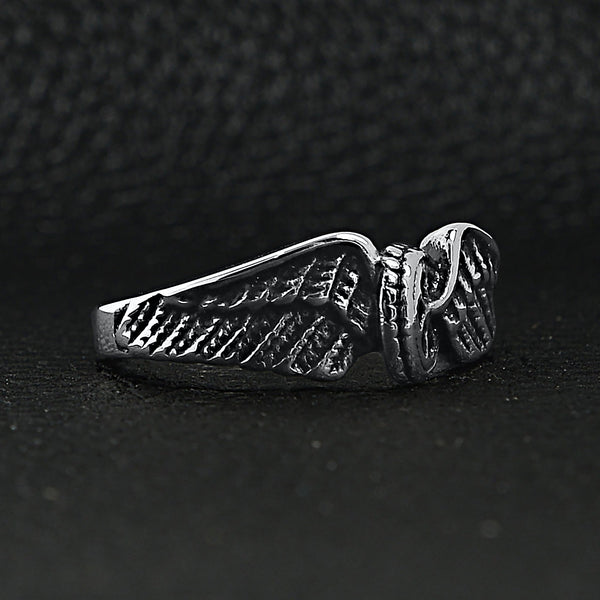 Stainless steel polished winged wheel ring angled on a black leather background.