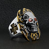 Stainless steel red Cubic Zirconia eyed flaming skull with 18K gold PVD Coated accents and Maltese Cross ring angled on a black leather background