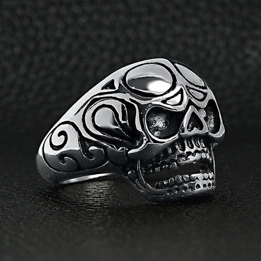 Stainless steel polished filigree skull ring angled on a black leather background.