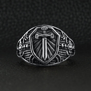 Stainless steel medieval sword and shield ring on a black leather background.