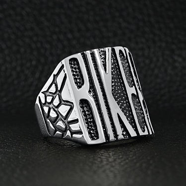 Stainless steel polished "BIKER" men's ring angled on a black leather background.
