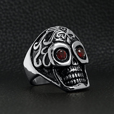 Stainless steel polished red Cubic Zirconia eyed filigree skull ring angled on a black leather background.