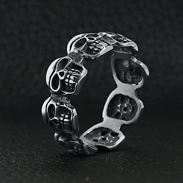 Stainless steel polished multi skull ring upright on a black leather background.