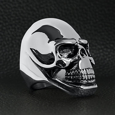 Stainless steel grinning skull ring angled on a black leather background.