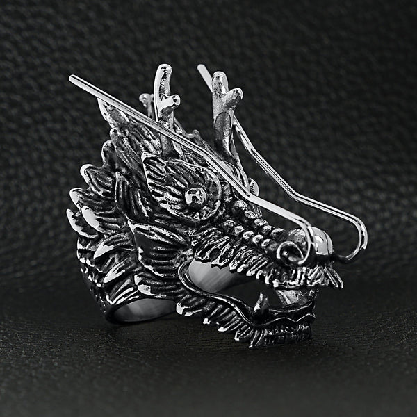 Stainless steel eastern luck dragon head ring angled on a black leather background.