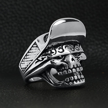 Stainless steel trucker hat skull ring angled on a black leather background.