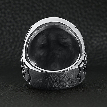 Stainless steel skull with skeleton accents ring back view on a black leather background.
