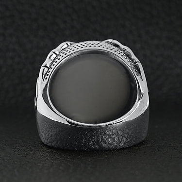 Stainless steel skeleton hands holding blue eyeball ring back view on a black leather background.