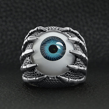 Stainless steel skeleton hands holding blue eyeball ring on a black leather background.
