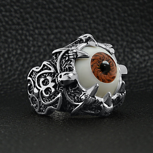 Stainless steel gothic red eyeball with claw and skull accents ring angled on a black leather background.
