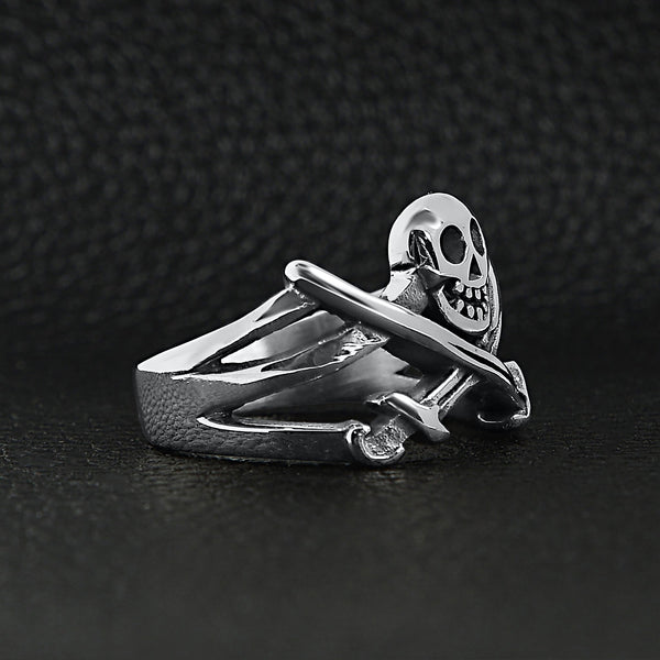 Stainless steel pirate Jolly Roger skull with crossed swords ring angled on a black leather background.