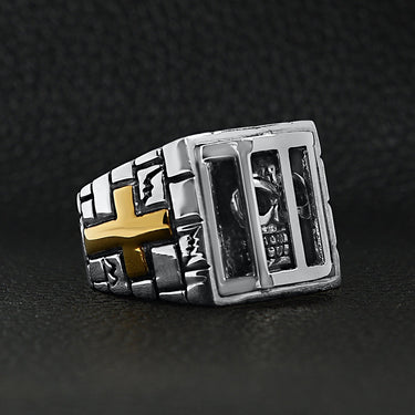 Stainless steel medieval jailed skull with 18K gold PVD Coated Cross accents ring angled on a black leather background.