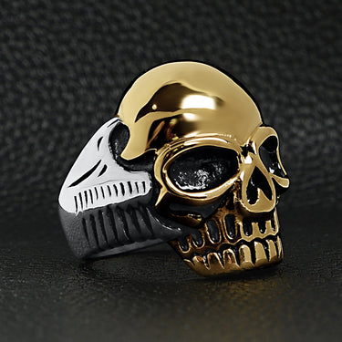 Stainless steel and 18K gold PVD Coated skull ring angled on a black leather background.