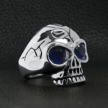 Stainless steel blue Cubic Zirconia eyed cracked skull ring angled on a black leather background.