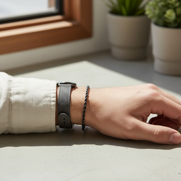 Hand wearing a watch and bracelet on a light surface with plants in the background