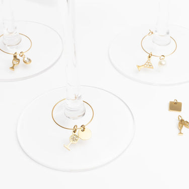 Gold wine glass charms with various charms on a white background