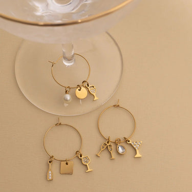 Gold wine glass charms with various charms on a beige background