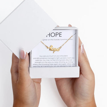 Gold Hope Necklace Gift Set in a white box held by hands with light pink nail polish.