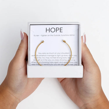 Gold Adjustable Cuff with Cancer Ribbon Charm GIft Set in a box with 'HOPE' text held by hands on a white background