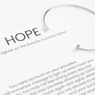 Silver Adjustable Cuff with Cancer Ribbon Charm GIft Set on a piece of paper with motivational text and the word 'HOPE'.