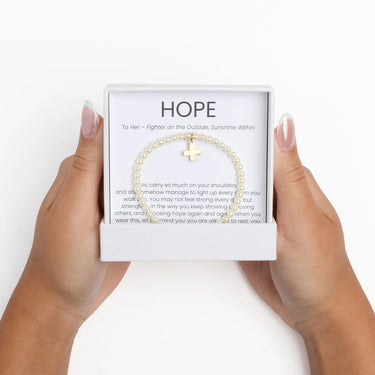Gold Pearl Beaded Bracelet with Cross Gift Set with cross charm held in front of a 'HOPE' message card on a white background
