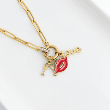 Gold necklace with red lip charm and 'love' pendant on a white background