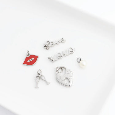 Collection of silver charms including a red lip, letter 'A', heart, and pearl on a white background