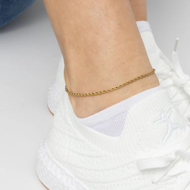 Gold anklet on a person's ankle with white sneakers on a light background