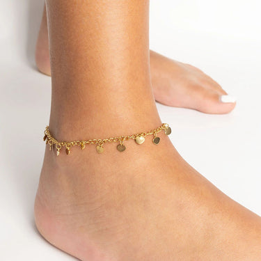 Gold anklet with heart charms on a foot against a light background