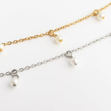 Two pearl necklaces, one gold and one silver, on a white background.