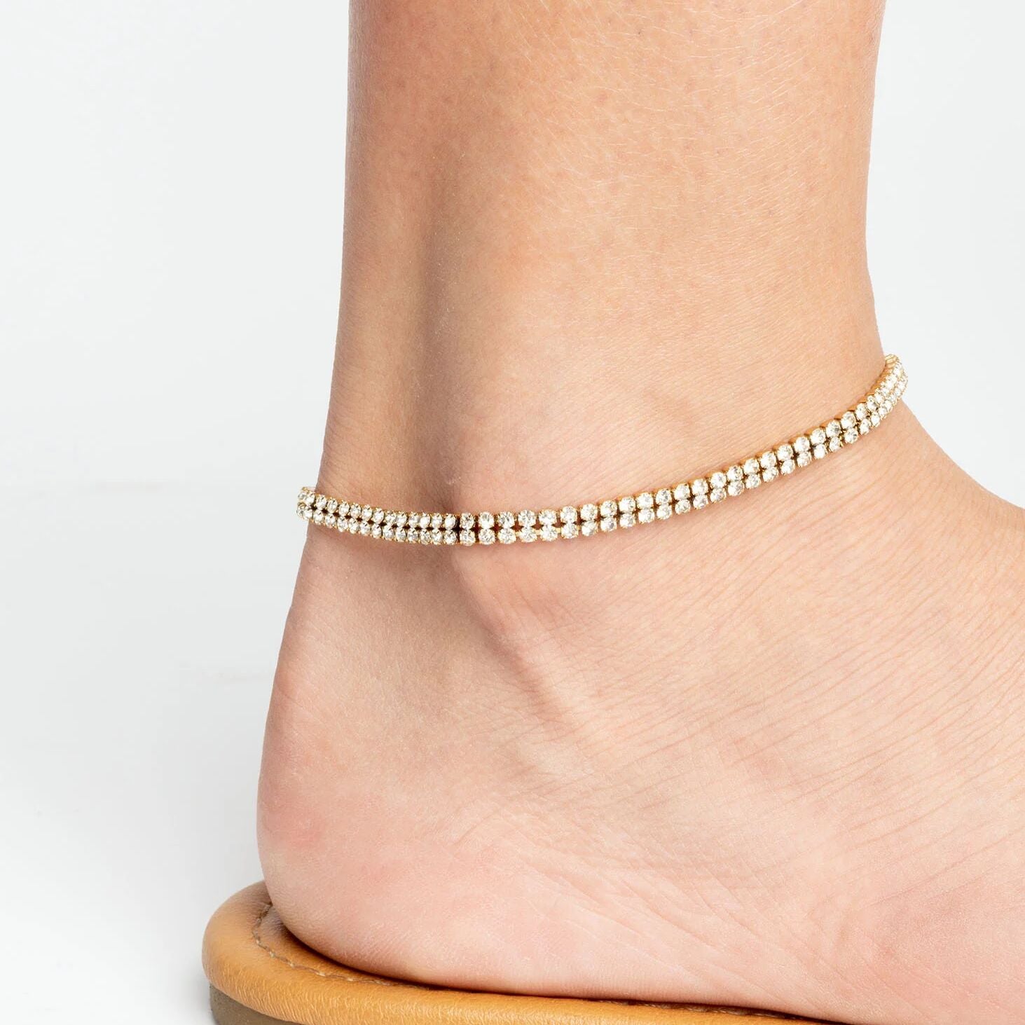 Gold anklet on a foot against a white background