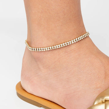Gold anklet on a foot with a plain background