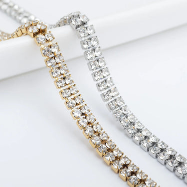 Two gold and silver bracelets with clear gemstones on a white background