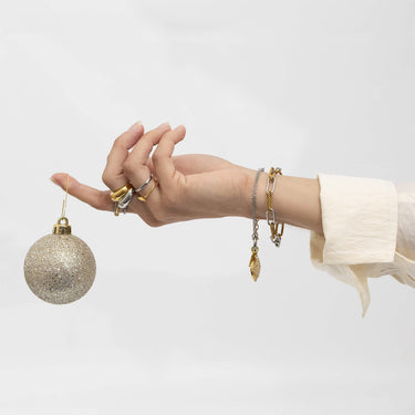 Hand holding a glittery gold ornament with multiple bracelets on a light gray background