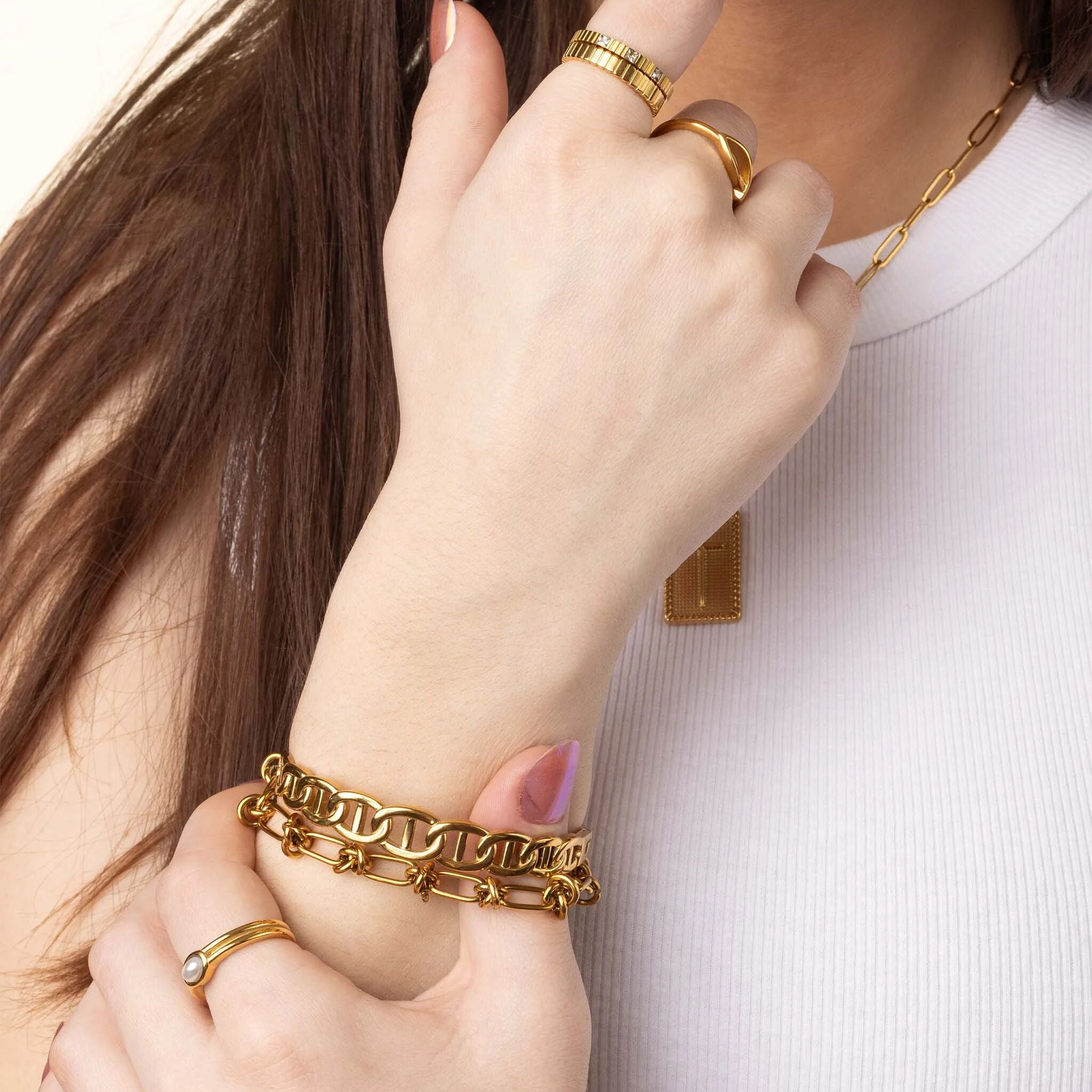 Close-up of a person wearing gold jewelry including a bracelet, ring, and necklace on a plain background.