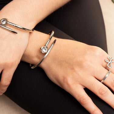 Close-up of a wrist wearing multiple silver bracelets and rings on a dark background