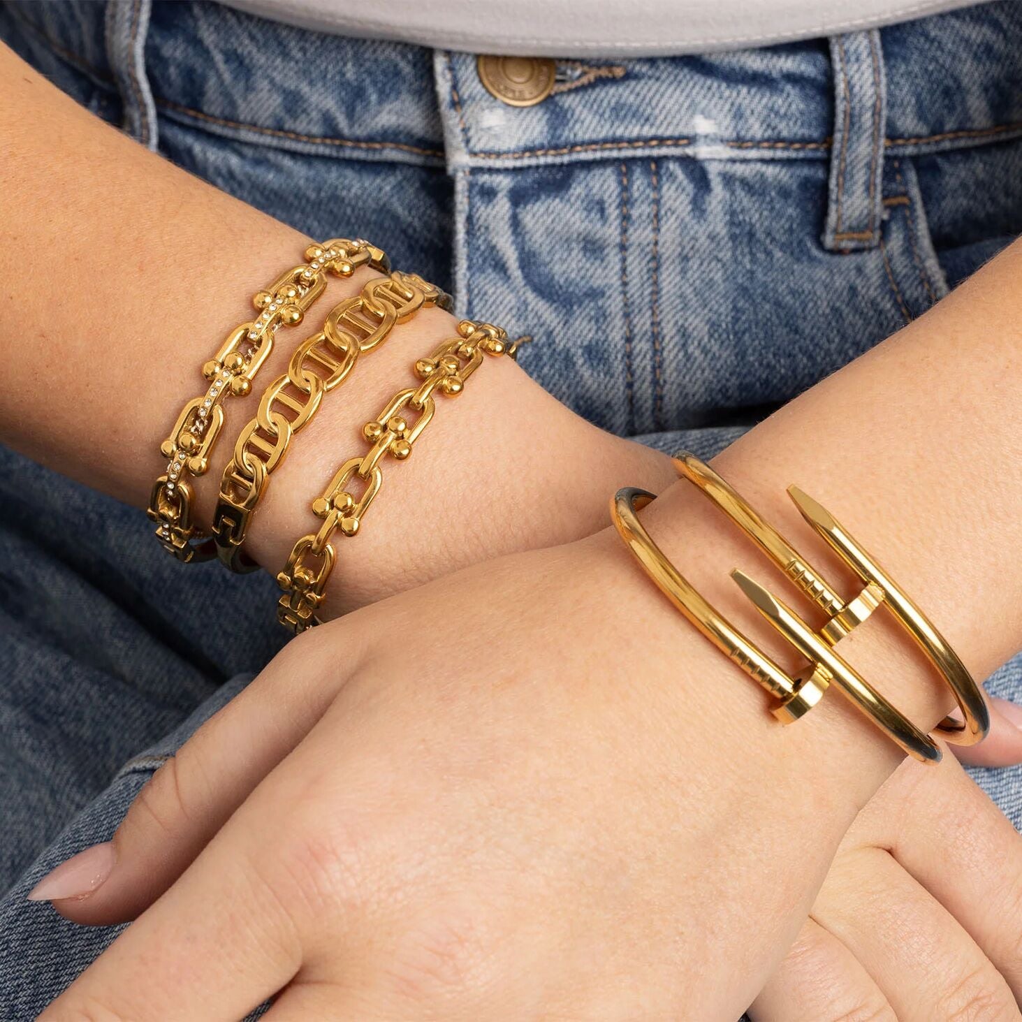 Gold chain bracelet and cuff on a wrist with denim background