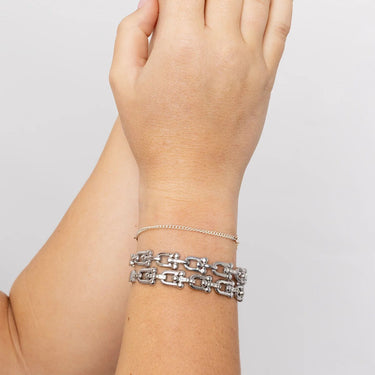 Silver bracelet on a wrist against a plain background