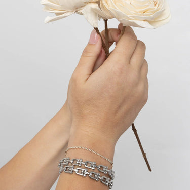 Hand holding a bouquet of flowers with silver bracelets on a plain background