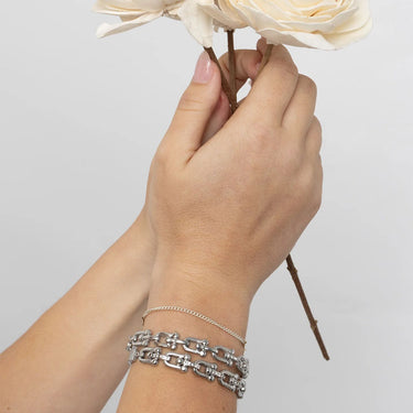 Hand holding flowers with silver bracelets on a plain background