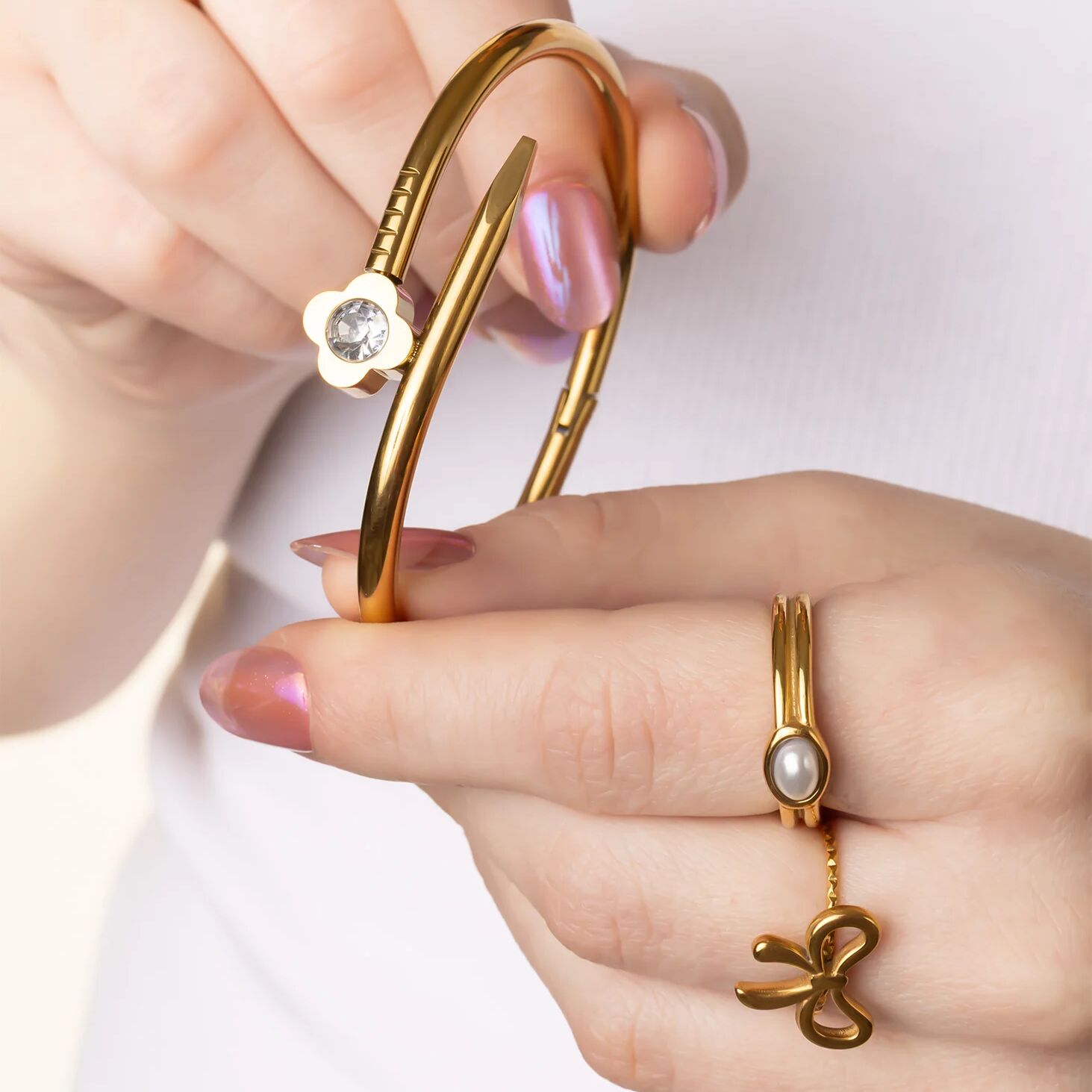 Gold bangles with pearl and gemstone accents held by a hand against a white background