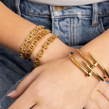 Gold chain bracelet and bangle on a wrist with denim background