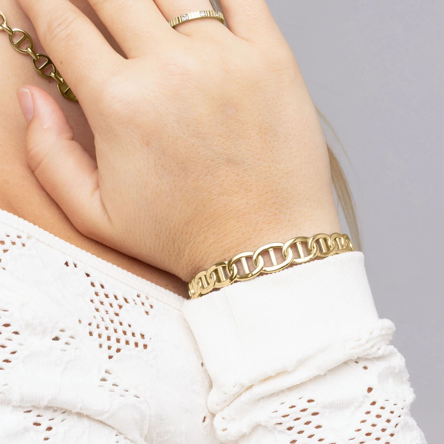Gold bracelet on a hand with a white lace garment against a gray background