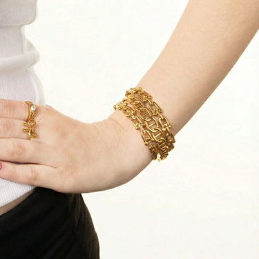 Gold bracelet on a wrist with a plain background