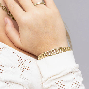 Gold bracelet on a hand with a white lace garment against a gray background
