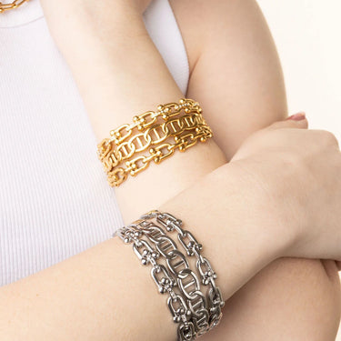 Two gold and one silver chain bracelet on a person's wrist against a white background