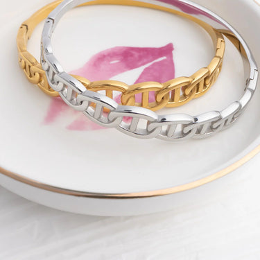 Two gold and silver bracelets on a white dish with a pink flower.