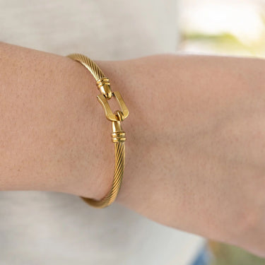 Gold buckle clasp bracelet on a wrist with a blurred background