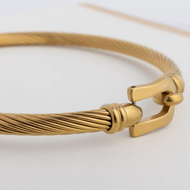 Gold bracelet with a buckle clasp on a light gray background