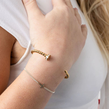Close-up of a person's wrist wearing gold bracelets on a plain background